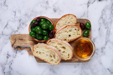 Aperatif, dilimlenmiş ciabatta ekmeği, zeytinyağı, yeşil zeytin, Chalkidiki zeytinleri, klasik yeşil zeytin, mermer bir masada, üst manzara, insan yok.,