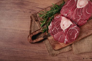 Kemiklerdeki eklem, ossobuko için çiğ et, ahşap kesim tahtası, biberiye filizi, baharatlar, üst manzara, insan yok.,