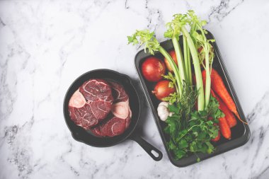 Kemikte bilek, ossobuko için çiğ et, dökme demir bir tavada, sebzeli pişirme çarşafı, üst manzara, insan yok.,