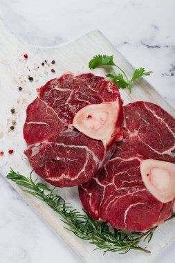 Kemiklerdeki eklem, ossobuko için çiğ et, ahşap kesim tahtası, biberiye filizi, baharatlar, üst manzara, insan yok.,