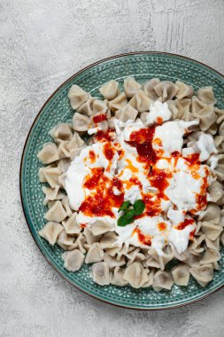 Tabakta, üzerinde kadife yoğurt ve yeşil aksanlı güzel hazırlanmış bir tabakta sergilenen baharatlı kırmızı sos bulunan bol miktarda Türk hamur köftesi yer alıyor..