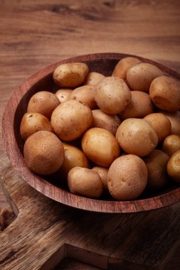 Small, unpeeled potatoes gathered together in a rustic wooden bowl, highlighting their earthy texture and natural colors against a warm wooden backdrop. clipart