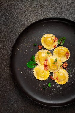Taze ravioli, tereyağlı, baharatlı ve otlu, kızarmış domuz pastırmalı, siyah tabakta, üst manzara, koyu arka plan, insan yok.,