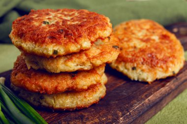 Crispy potato pancakes Latkes, stacked on a wooden board next to fresh green onions, natural light, homemade, no people, clipart