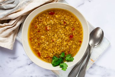 Çerçeveyi dolduran dumanı tüten bir mercimek çorbası, kırmızı biber parçaları ve taze kişniş filizi ile zengin altın bir çorba sergiliyor..