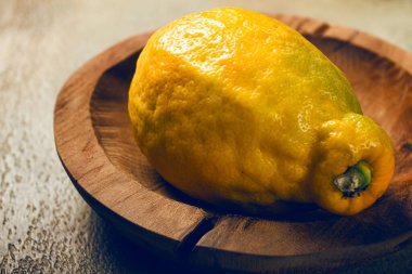 Canlı bir limon kırsal bir ahşap tabakta oturur. Yumuşak ışık dokusunu ve rengini vurgulayarak ev mutfağında sıcak bir atmosfer yaratıyor..