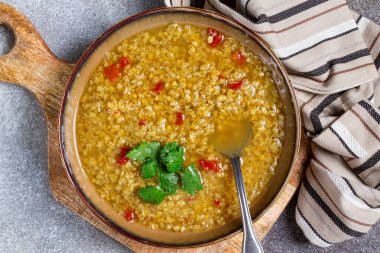 Baharatla tatlandırılmış ve doğranmış domatesler ve taze kişniş ile süslenmiş lezzetli tahıl tabağıyla dolu bir köy kasesi. Taş bir yüzey üzerinde desenli bir bez peçetenin yanında servis edilmiş..