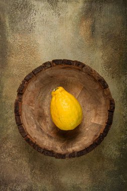 Tek bir sarı meyve, canlı rengini dokulu bir arka plana karşı sergiliyor ve kırsal ahşap bir kasede dinleniyor. Düzenleme doğal güzelliği ve basitliği vurguluyor..
