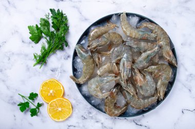 Taze çiğ karides, limon ve mermer bir yüzeyde kişniş dilimleri ile buza yayılmış, pişirmeye hazır, insan yok.