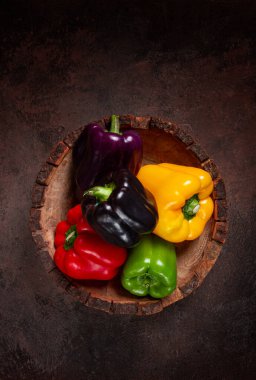 Ahşap bir kasede, koyu bir yüzeyde, renkli dolmalık biber koleksiyonu.