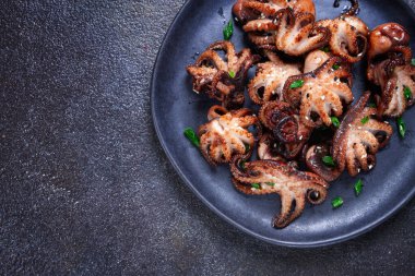 Izgara bebek ahtapot, çubuklarla servis ediliyor, siyah bir tabakta, ev yapımı, insan yok.,