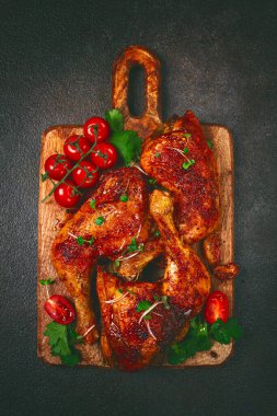Kızarmış tavuk bacağı, taze kiraz domatesleri ve ahşap kesim tahtasıyla servis edilen otlar, ev yapımı, insan yok.,