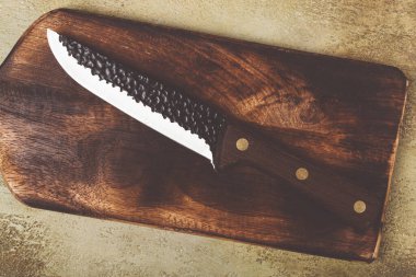İyi işlenmiş bir mutfak bıçağı eşsiz bir doku ve tahıl içeren ahşap bir kesim tahtasının üzerinde yatar. Bıçağın keskin bıçağı ve sapı işlevselliğini ve estetik çekiciliğini ön plana çıkarıyor..