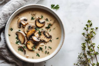 Dilimlenmiş mantarlar ve taze otlarla süslenmiş kremalı mantar çorbasıyla dolu bir kase mermer tezgahta oturup yemek için sıcak ve davetkar bir atmosfer yaratır..