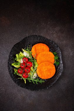 Kızarmış balık pirzolası, balık köftesi, siyah tabakta, taze marul yaprakları, roka ve kiraz domatesleri, ev yapımı, insan yok.,