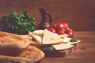 Gürcistan usulü dilimlenmiş peynir, ahşap bir doğrama tahtasında, domatesli otlar ve lavaşla, kırsal tarzda, Gürcü mutfağı, insan yok.