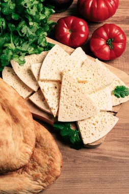 Gürcistan usulü dilimlenmiş peynir, ahşap bir doğrama tahtasında, domatesli otlar ve lavaşla, kırsal tarzda, Gürcü mutfağı, insan yok.