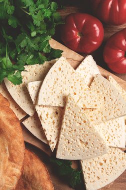 Gürcistan usulü dilimlenmiş peynir, ahşap bir doğrama tahtasında, domatesli otlar ve lavaşla, kırsal tarzda, Gürcü mutfağı, insan yok.