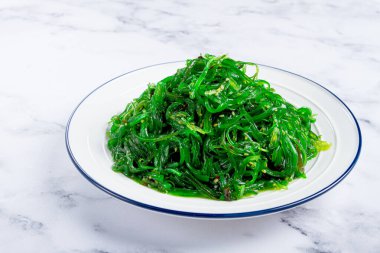 Chuka salatası taze yosundan yapılmış, susam soslu, beyaz tabakta servis ediliyor, insan yok.,