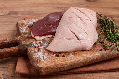 Taze çiğ ördek göğsü, ahşap kesim tahtasının üzerinde, bitkiler ve baharatlarla, insan yok.