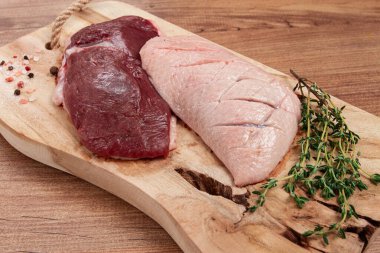 Taze çiğ ördek göğsü, ahşap kesim tahtasının üzerinde, bitkiler ve baharatlarla, insan yok.