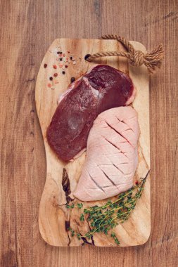 Taze çiğ ördek göğsü, ahşap kesim tahtasının üzerinde, bitkiler ve baharatlarla, insan yok.