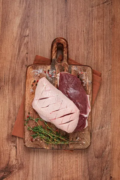 Taze çiğ ördek göğsü, ahşap kesim tahtasının üzerinde, bitkiler ve baharatlarla, insan yok.