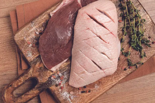 Taze çiğ ördek göğsü, ahşap kesim tahtasının üzerinde, bitkiler ve baharatlarla, insan yok.