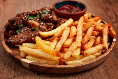 Barbekü tavuk kanatları, susam tohumları serpiştirilmiş, patates kızartması ve sos, ahşap bir tabakta, köy usulü.,