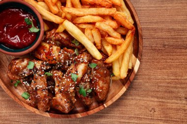 Barbekü tavuk kanatları, susam tohumları serpiştirilmiş, patates kızartması ve sos, ahşap bir tabakta, köy usulü.,
