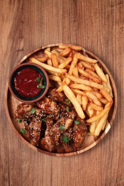 Barbekü tavuk kanatları, susam tohumları serpiştirilmiş, patates kızartması ve sos, ahşap bir tabakta, köy usulü.,