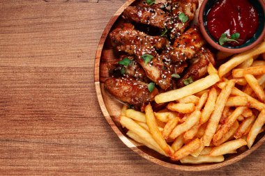 Barbekü tavuk kanatları, susam tohumları serpiştirilmiş, patates kızartması ve sos, ahşap bir tabakta, köy usulü.,