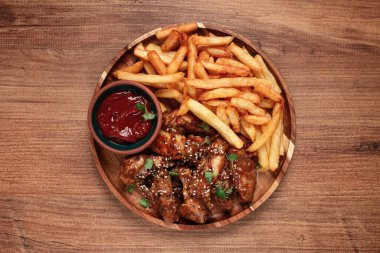 Barbekü tavuk kanatları, susam tohumları serpiştirilmiş, patates kızartması ve sos, ahşap bir tabakta, köy usulü.,