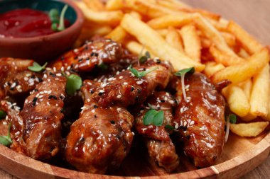 Barbekü tavuk kanatları, susam tohumları serpiştirilmiş, patates kızartması ve sos, ahşap bir tabakta, köy usulü.,
