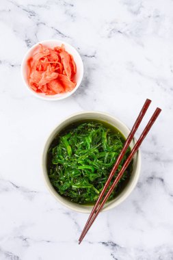 Chuka salatası, taze deniz yosunundan yapılmış, susam soslu, beyaz bir kasede, çubuklu ve turşulu zencefilli, insanlar olmadan.,