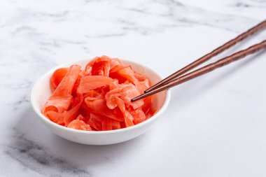 Turşulu zencefil, çubuklu, küçük beyaz bir kasede, mermer bir tezgahta, yakın plan, insan yok.,