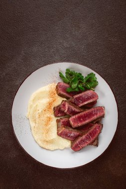 Dilimlenmiş biftek, kremalı patates püresi ve taze otlarla servis edilir.
