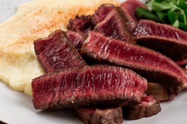 Dilimlenmiş biftek, kremalı patates püresi ve taze otlarla servis edilir.