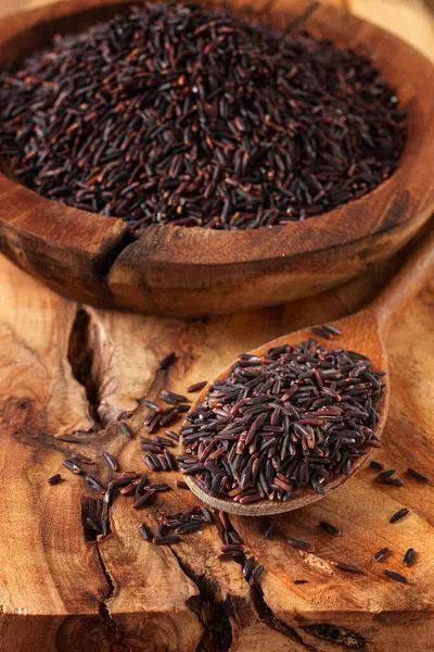 Tahta bir kâse içinde doğal siyah pirinç ve tahta bir yüzey üzerinde kırsal tarzda kaşık.