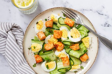 Lezzetli somon balığı ve yumurta salatası, öğle yemeğinde taze salatalık ve şifalı bitkilerle servis edilir.