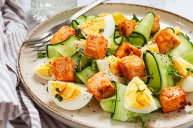 Lezzetli somon balığı ve yumurta salatası, öğle yemeğinde taze salatalık ve şifalı bitkilerle servis edilir.