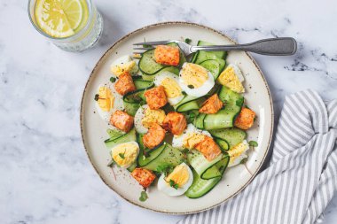 Lezzetli somon balığı ve yumurta salatası, öğle yemeğinde taze salatalık ve şifalı bitkilerle servis edilir.