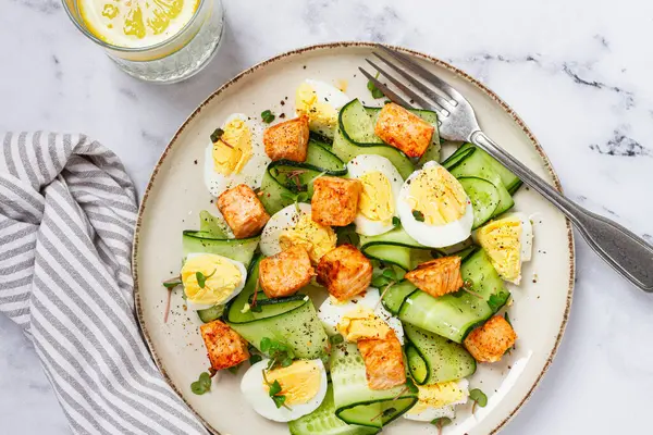 Lezzetli somon balığı ve yumurta salatası, öğle yemeğinde taze salatalık ve şifalı bitkilerle servis edilir.