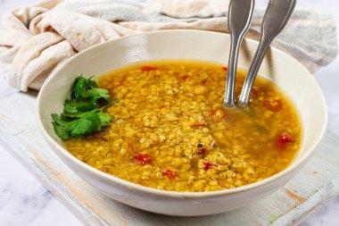 Zengin altın renginde mercimek çorbası kırsal bir kasede servis edilir. Çorba taze otlar ve baharatlar içeriyor, serin bir akşam için rahatlatıcı bir yemek haline getiriyor..