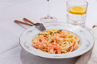 Karides ve kekikli makarna, beyaz bir tabakta servis ediliyor, bir bardak beyaz şarapla, masa hazır, gurme yemeği, keten masa örtüsü üzerinde, insan yok.,,