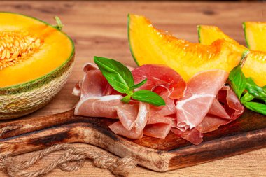 Kavun, prosciutto ve taze fesleğen, ahşap servis tahtasında, rustik tarzda.,