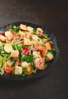 Kaplan karidesli sezar salatası, karides salatası, marul yaprağı, bıldırcın yumurtası, vişneli domates, parmesan peyniri, siyah tabakta.,