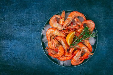 Buzlu taze donmuş karides, limon ve biberiyeli, koyu mavi bir masada, üst tarafta, insan yok.