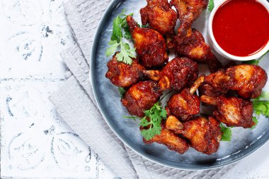 Kızarmış tavuk parçaları, soslu ve otlu bir tabakta, modern bir mutfak ortamında, hiç insan yok.