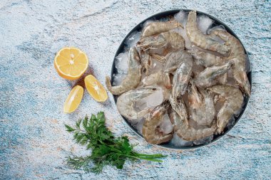 Taze çiğ karides, limon ve mermer bir yüzeyde kişniş dilimleri ile buza yayılmış, pişirmeye hazır, insan yok.